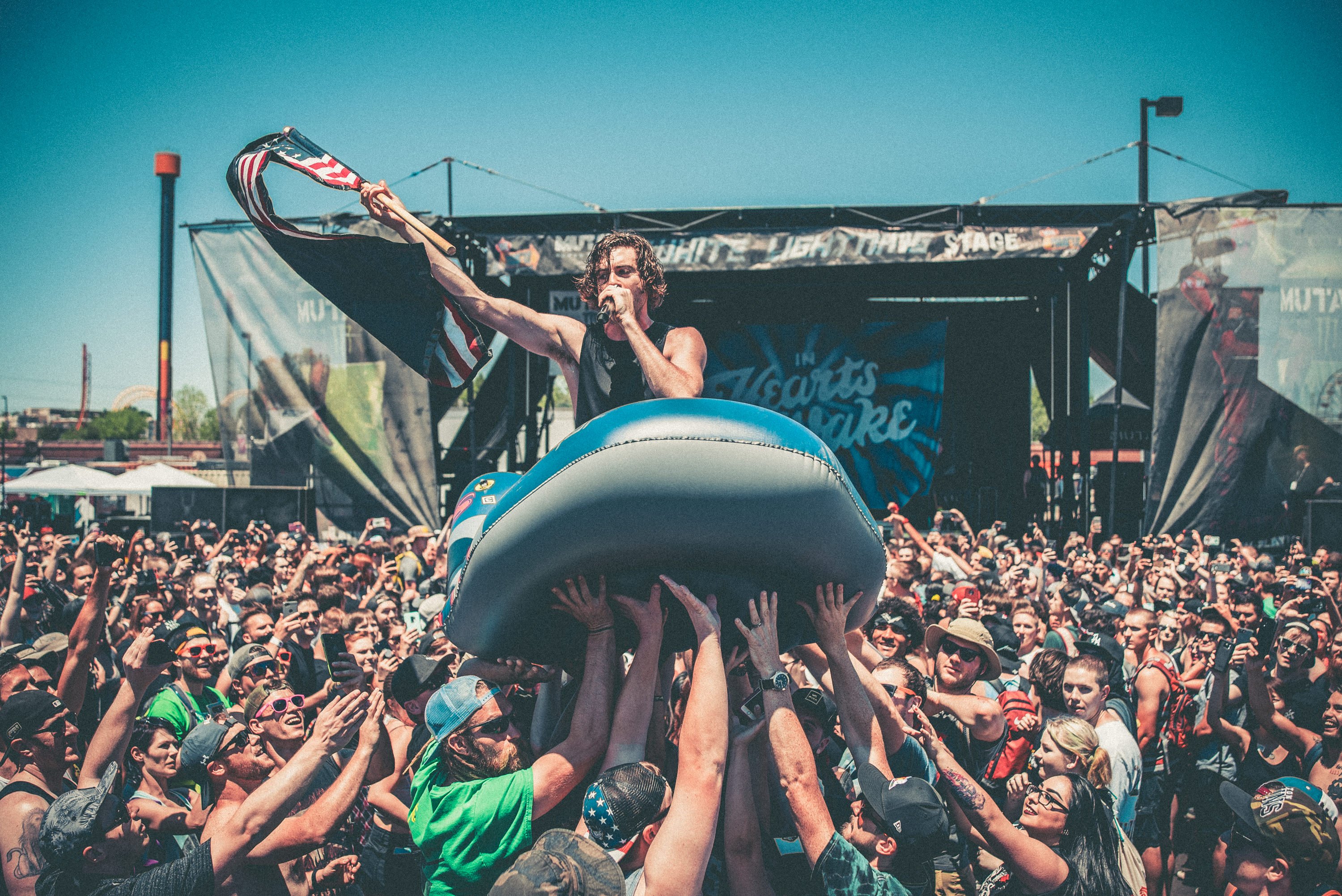 A performing artist holds up a flag while singing into a microphone and riding an inflatble boat above the crowd