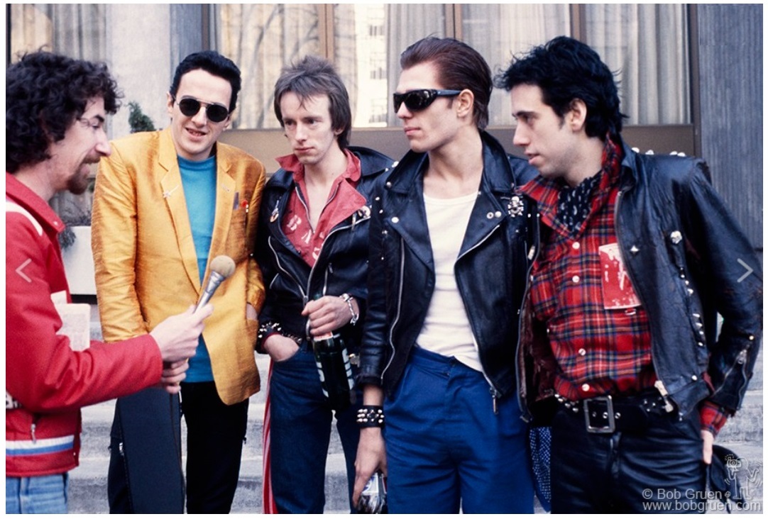 The Clash being interviewed during their tour of the USA. February 1979. This shows off their casual style with American 1950s leather jackets, patches, and plaid shirts in bright eye catching colors.