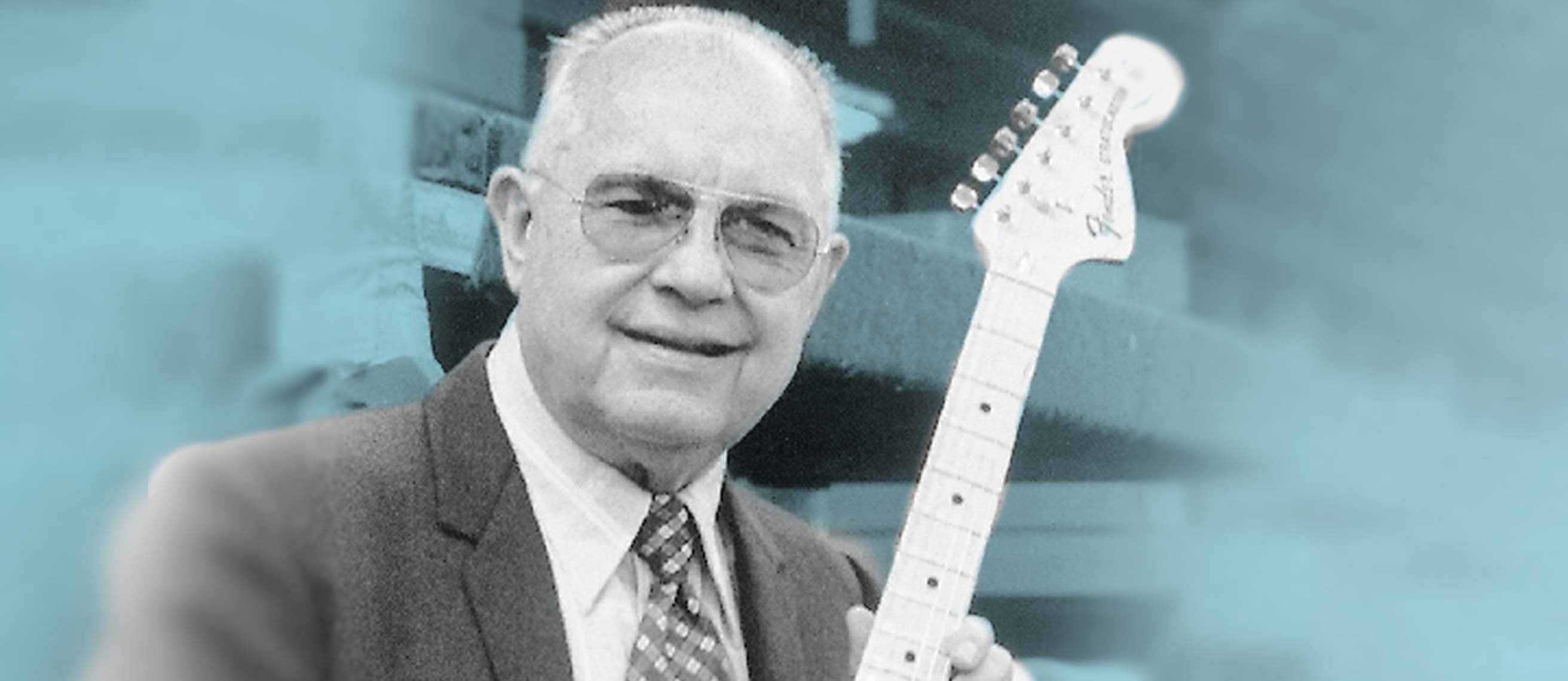 The late leo fender in a suit holding a guitar