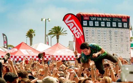 Man crowding surfing above a crowd of people with a inflatable bulletin in the background
