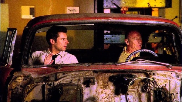 Screen shot of Shawn and Henry a car at the motor shop of their high school, referencing Sixteen Candles.