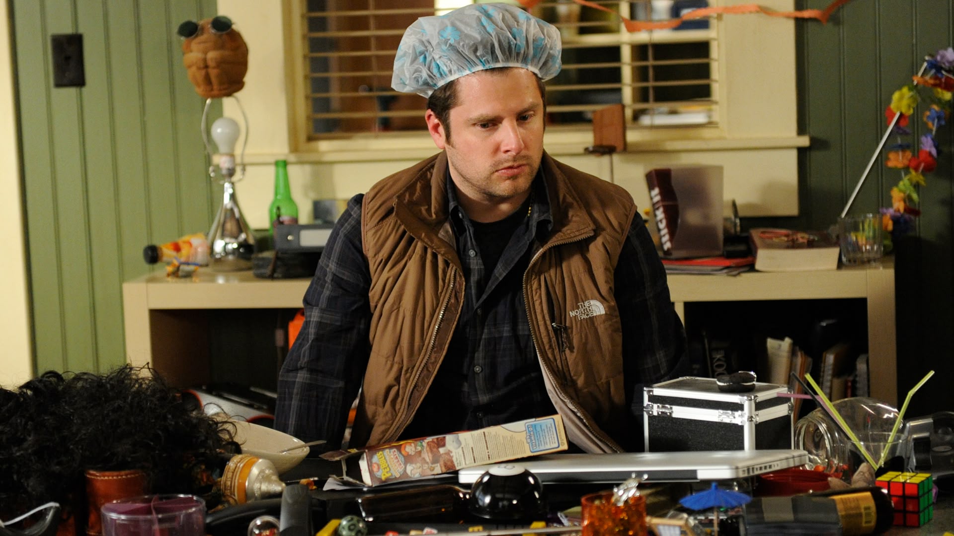 photo of Shawn Spencer at a desk in the Psych office wearing a shower cap looking confused