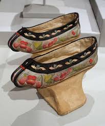 A pair of Chinese slippers from the 1800s embroidered with flowers and leaves, with a dark band of fabric at the top.