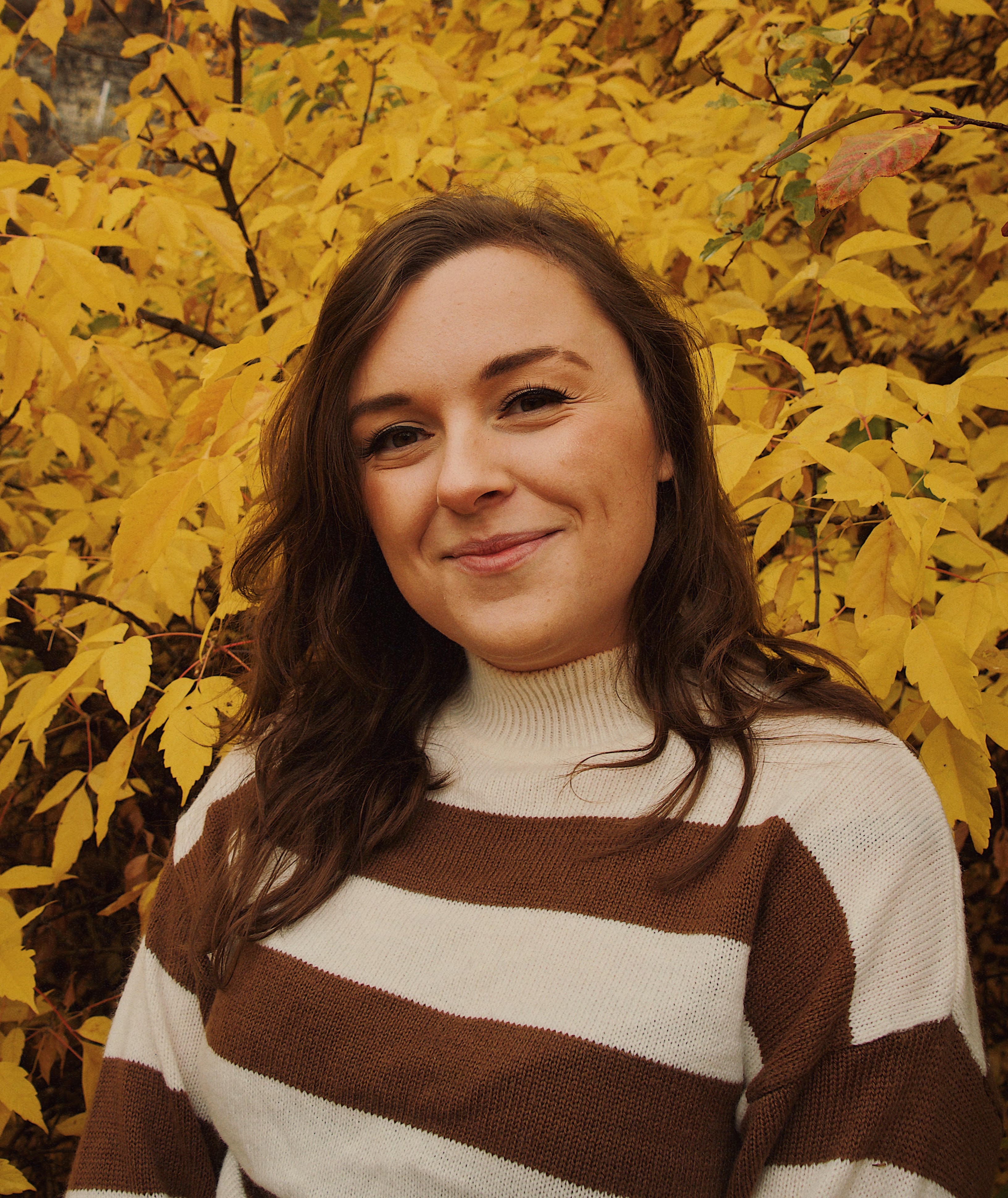 A photo of the article's author, Sydney Cazier, in a brown and white-striped sweater against a background of yellow leaves