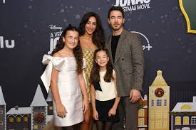 Event photo of a family of four dressed in semi-formal clothes, with two young girls standing in front of their parents and a decorated movie-themed backdrop behind them.