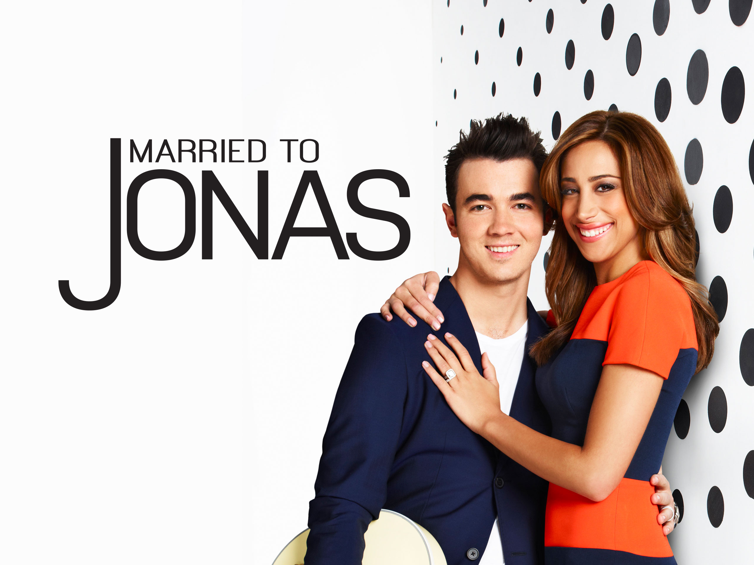 Promotional image with the title “Married to Jonas” beside a smiling couple standing in front of a white wall with large black polka dots, the woman hugging the man from the side and showing her wedding ring.