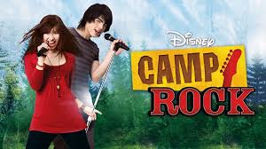 Disney movie poster featuring a girl in a red top and a boy behind her, both singing into microphones in front of a forest backdrop, with the title “Camp Rock.”