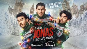 Holiday movie poster showing three men in matching green Christmas sweaters wrapped in colorful lights, standing in a snowy city street with the title “A Very Jonas Christmas Movie.”