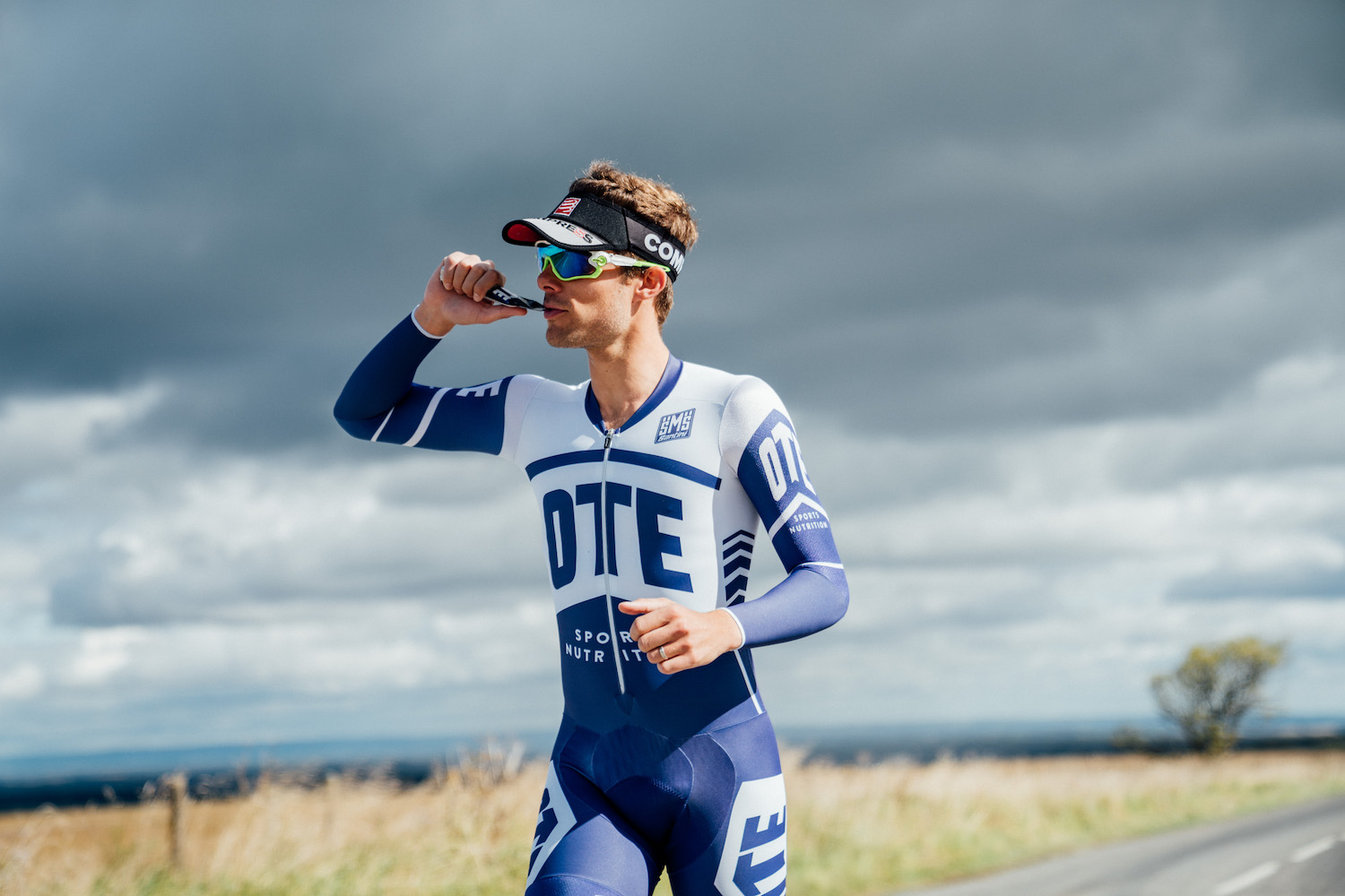 Photo of a man running in a triathlon suit while eating some kind of energy bar