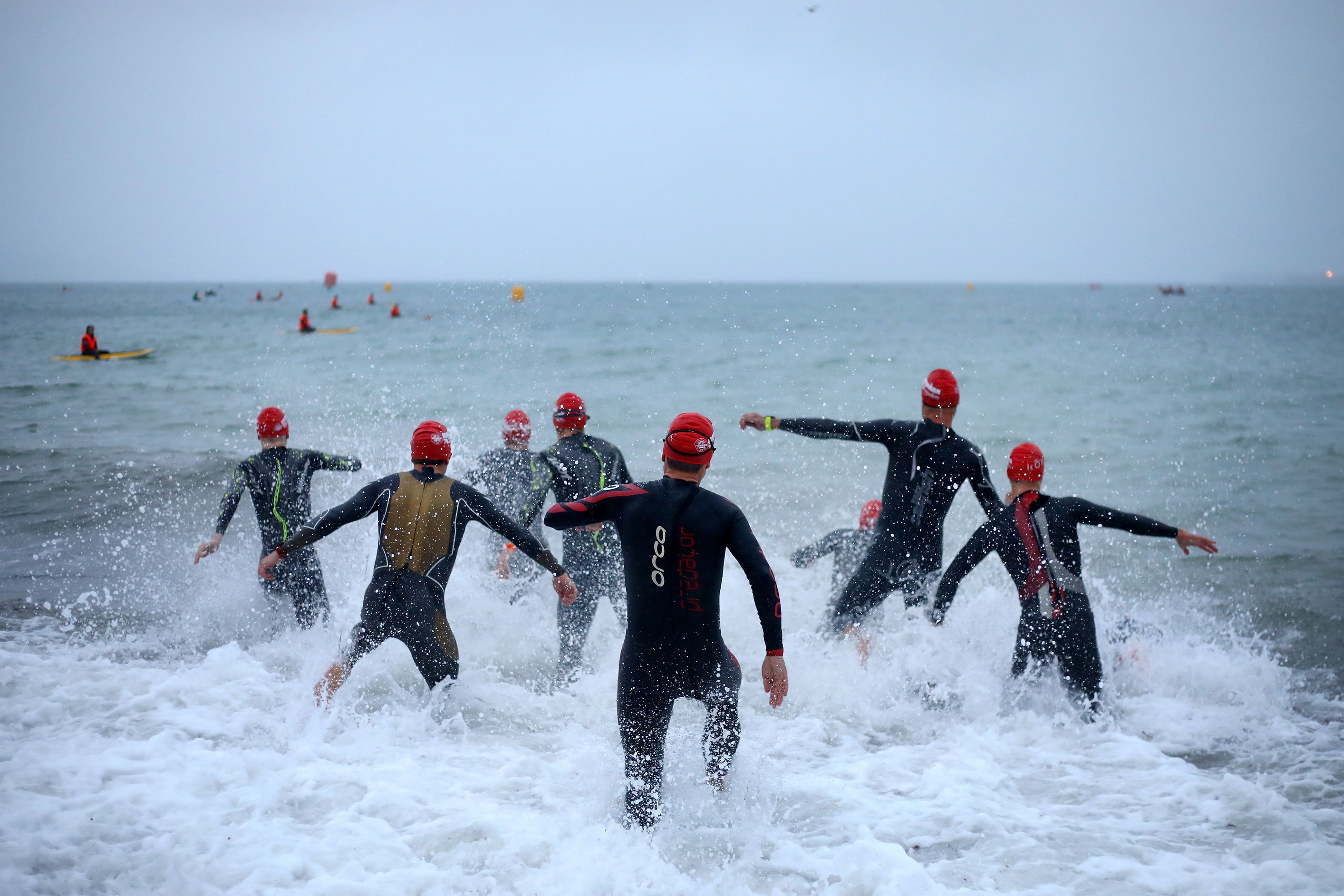 a group of 7 people running into the ocean wearing wet-suits and swim caps.