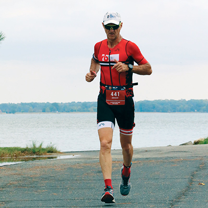 a man in a red triathlon suit running alongside a lake