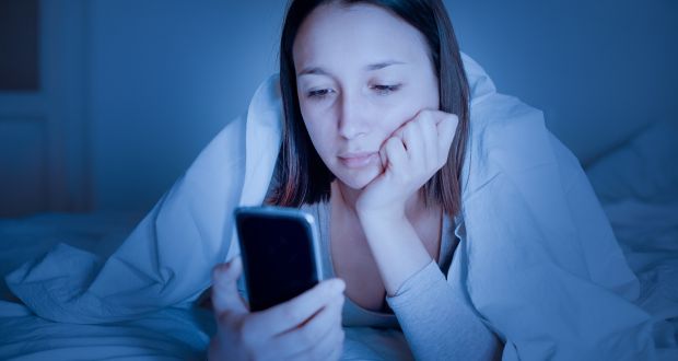 a distraught woman laying on a bed while staring at her phone 