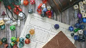 On a gray wood table sits a filled out D&D character sheet. Multiple dice sets of different colors surround the sheet along with the bags those dice come in.