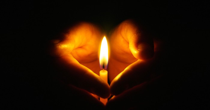 hands cupped in a heart shape around a lit candle