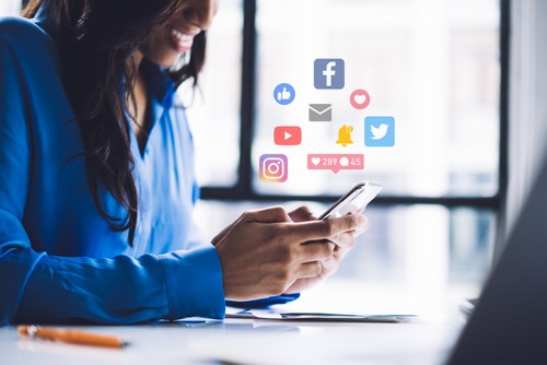 A woman smiling while on her phone, with social media icons coming out of her phone