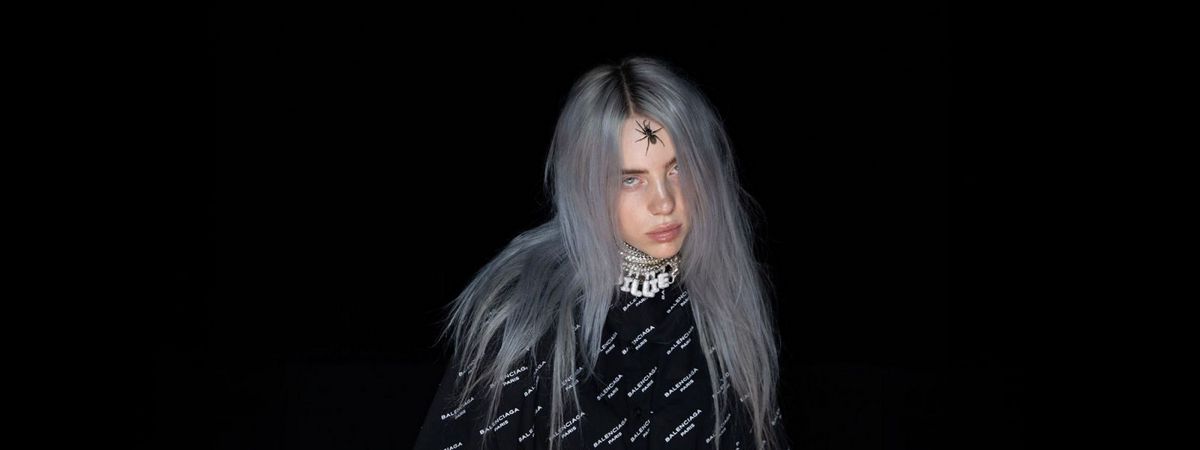 An image with Billie Eilish in the center. The background is black, contrasting Billie's grey-ish blue hair. She has a spider on her forehead and she's staring into the camera without a smile on her face