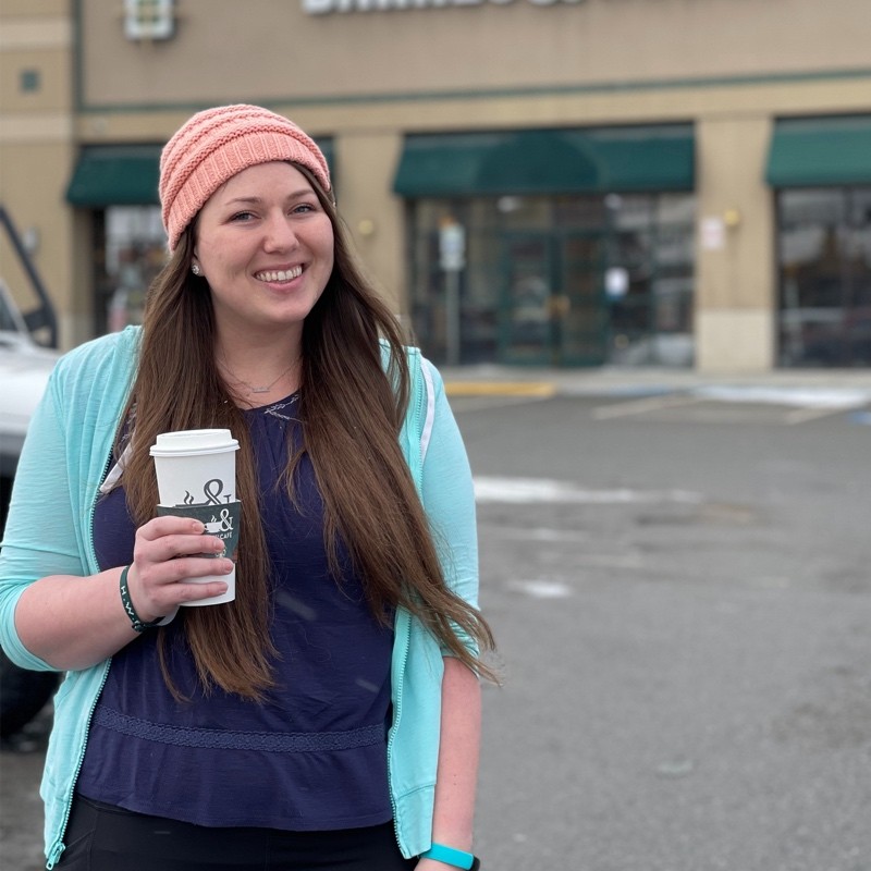 Melanie Hardman wearing a winter cap and smiling while she holds a warm drink in front of a bookstore in Alaska