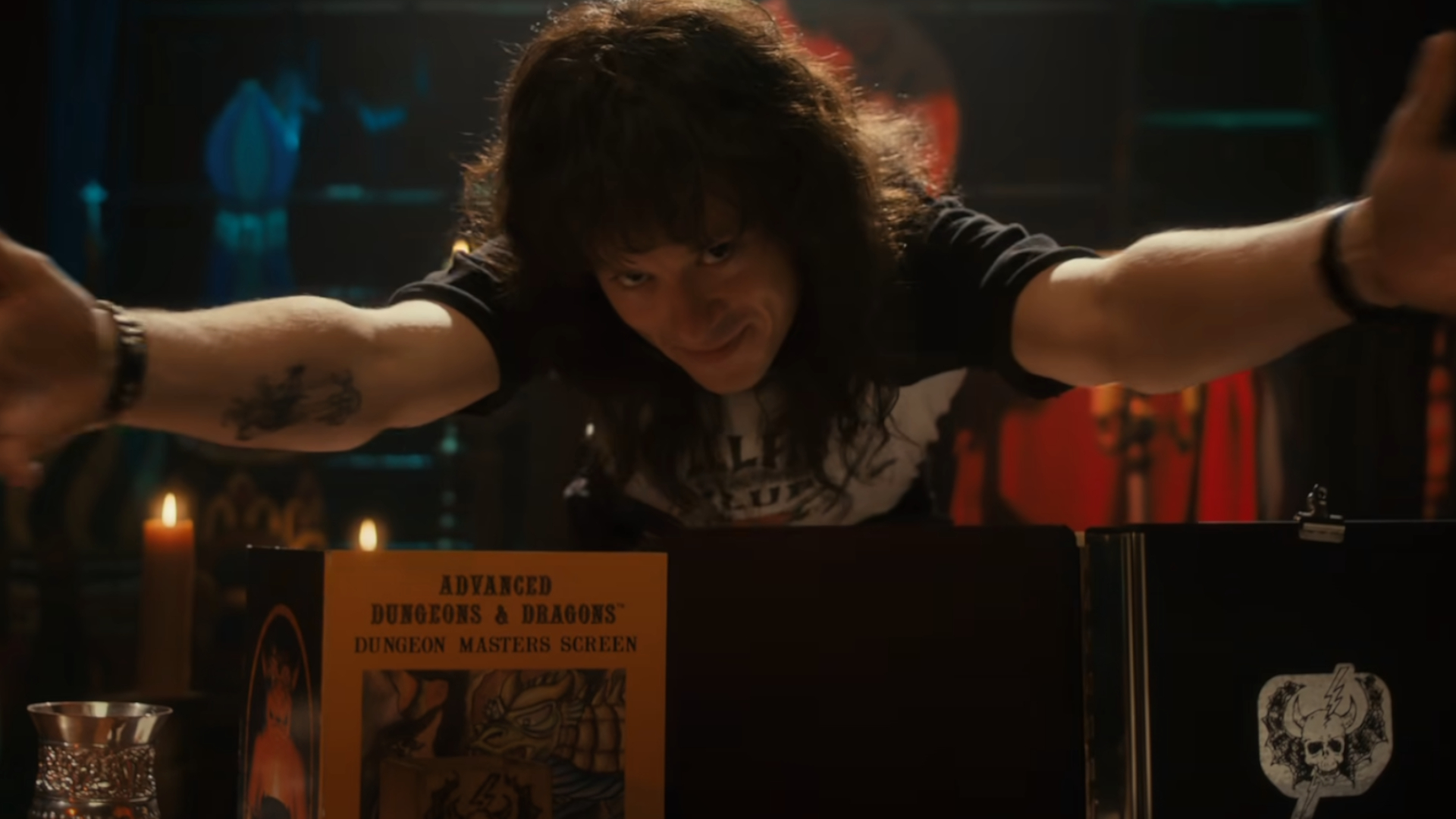 A young man with long curly dark hair leans over a propped up board that says Advanced Dungeons & Dragons. His arms are extended over the board.