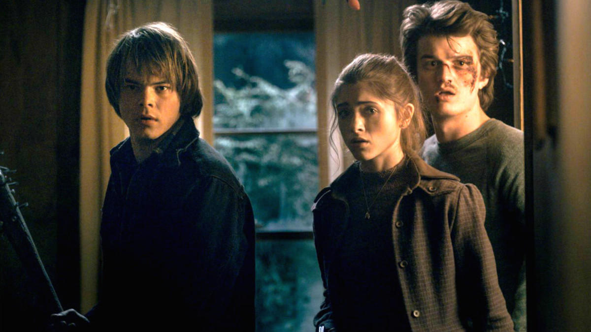 Three teenagers, a girl and two boys, stand ready for approaching danger. One holds up a bat with nails pounded into the end.