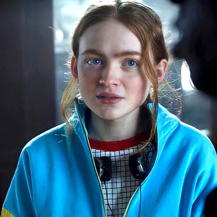 A red-haired teenage girl with headphones around her neck and a blue jacket.