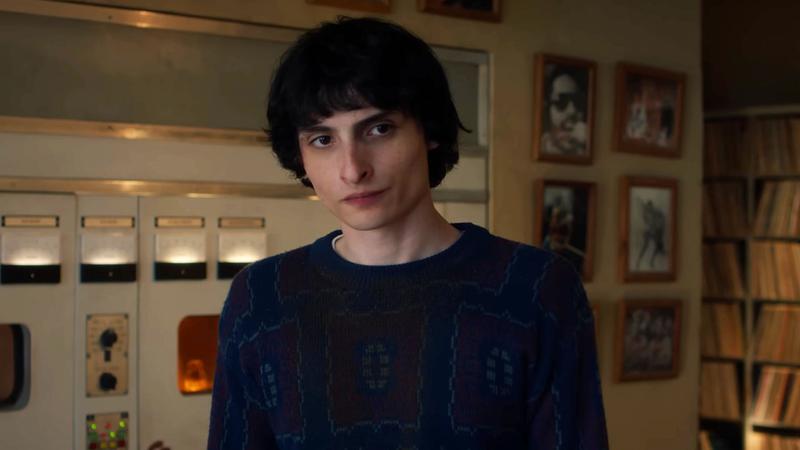 A black-haired teenage boy in a sweater looks across a room.