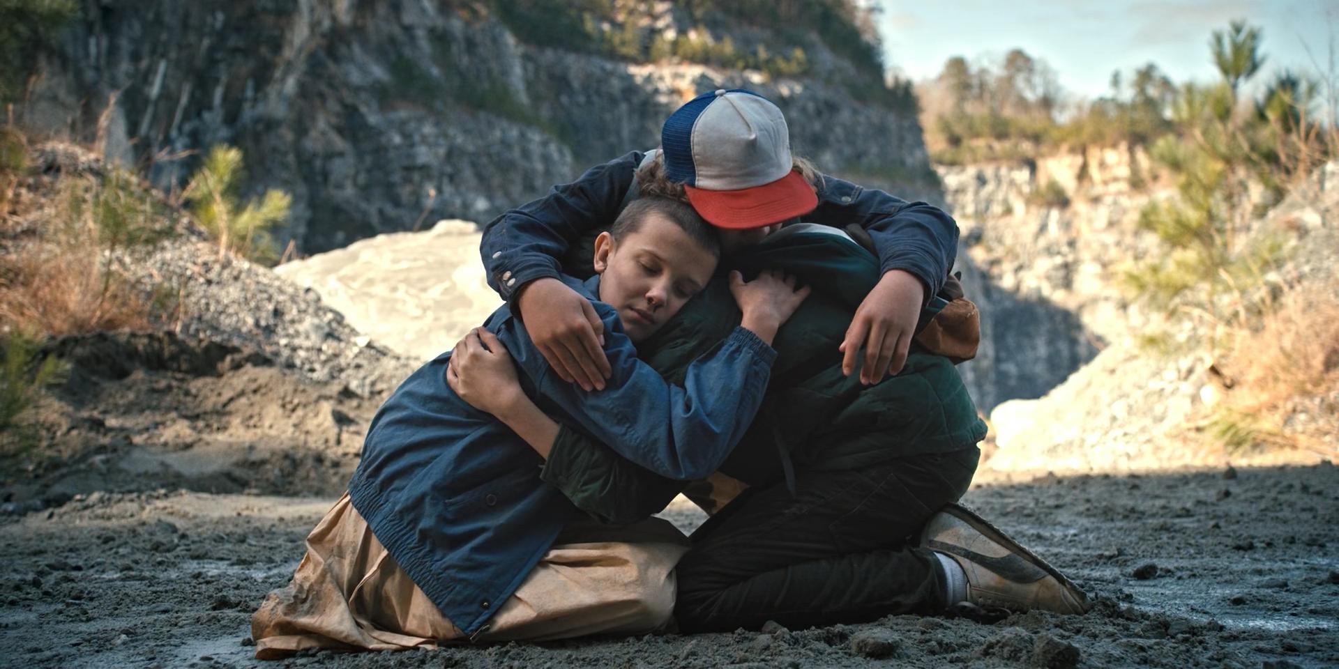 Three kids kneel on the ground, hugging each other in care and relief.