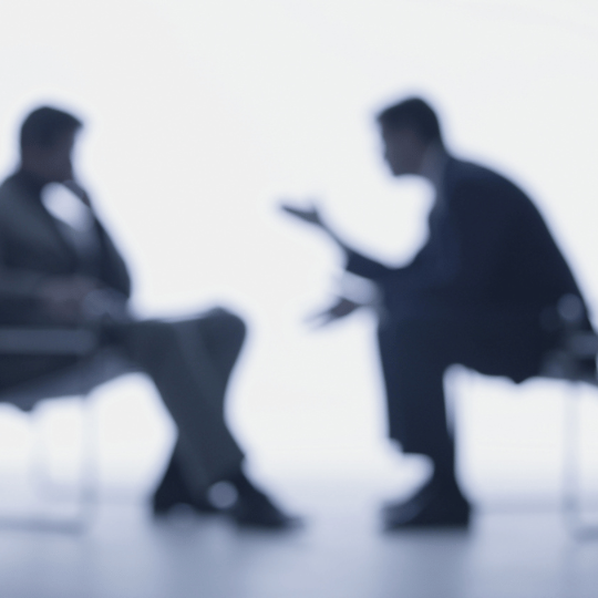 Two men sitting across from each other speaking to each other