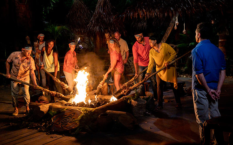 A group of Survivor castaways dipping their torches into fire.