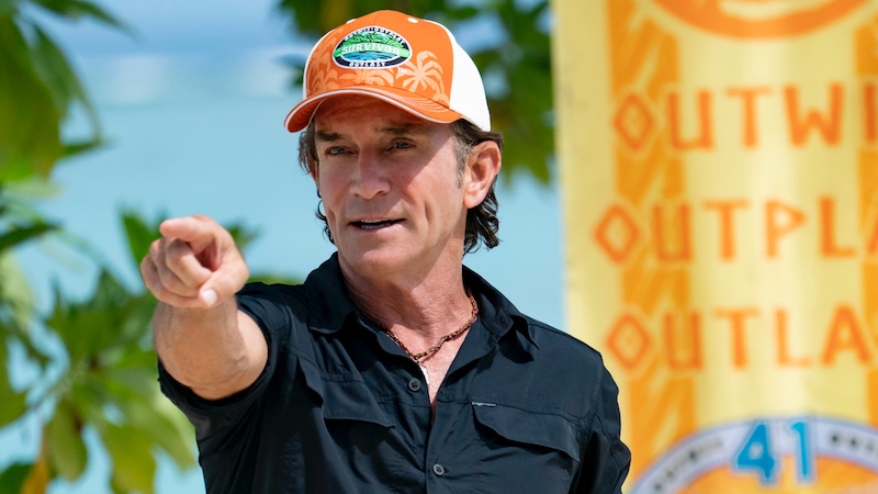 Jeff Probst wearing an orange hat pointing off in a distance.