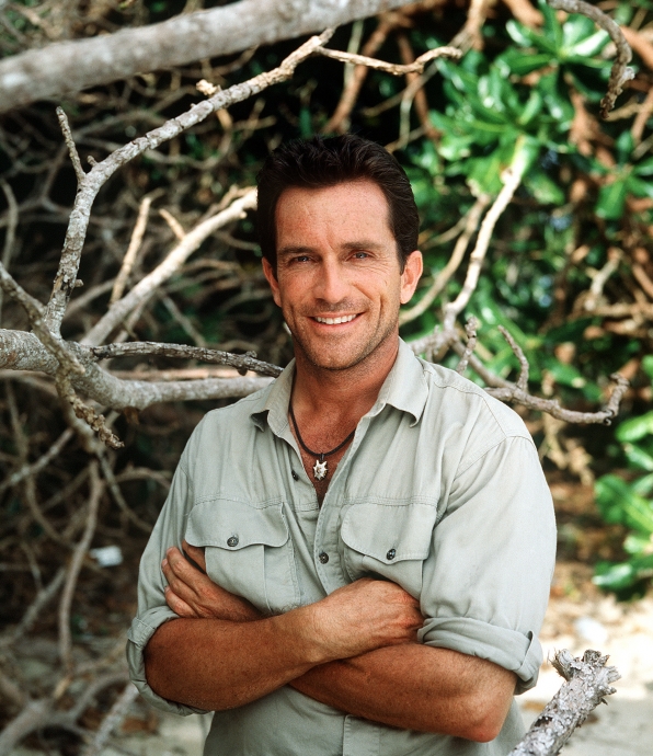 A young Jeff Probst standing on a beach with his arms folded.