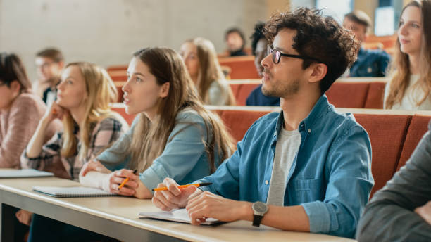 a group of students in a college class. 3 students in focus in the foreground and 7 students not in focus in the background.