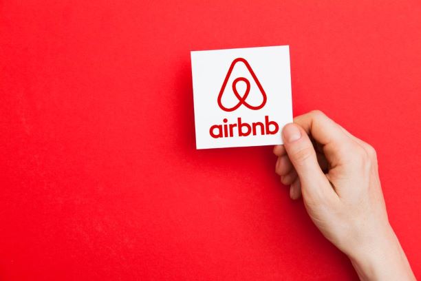 Bright red background with a hand holding a piece of paper with the Air BnB logo on it.