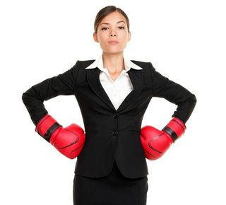 photo of a woman in a business skirt set wearing red boxing gloves with her hands on her hips and a stern look on her face