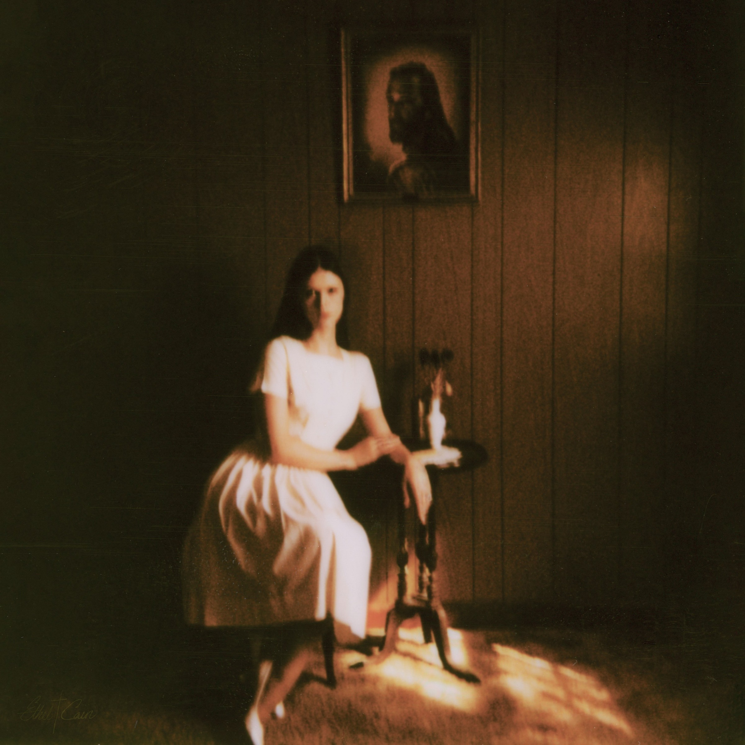 Album Cover art of Preacher's Daughter, a woman sits on a chair with samll end table with a picture of jesus on the wood planked wall