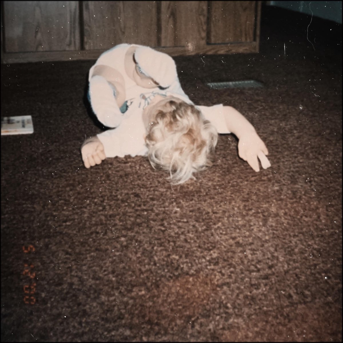 cover art for EP Carpet Bed, a young child plays on a carpet with their legs in the air, the childs face cannot be seen past their blonde shaggy hair