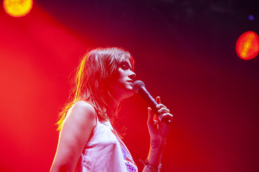 Ethel Cain perfroming at night covered in red lighting with microphone to her lips