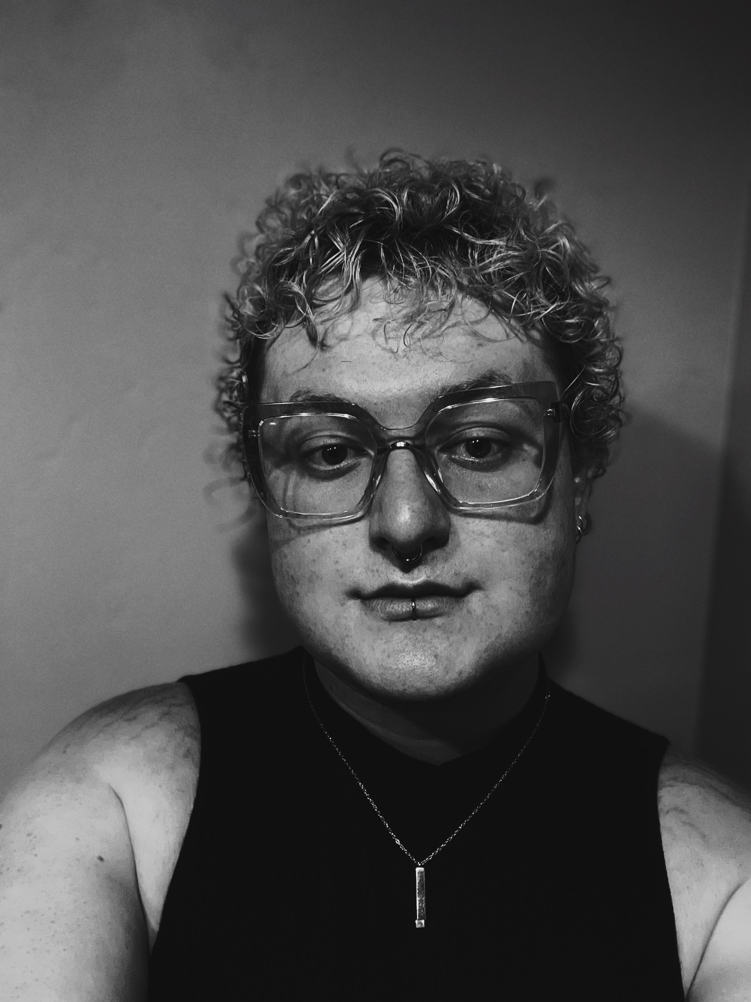 Black and White Headshot of Web Editor Prior Beaman-McGraw, Glasses, Curly hair, Mock neck turtle neck tanktop.