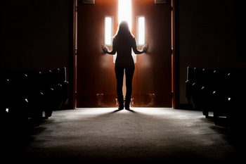 A silhouetted person walking out the doors of a church