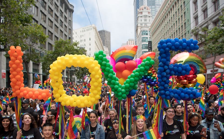 The word love spelled out in rainbow balloons surrounded by people at a pride parade