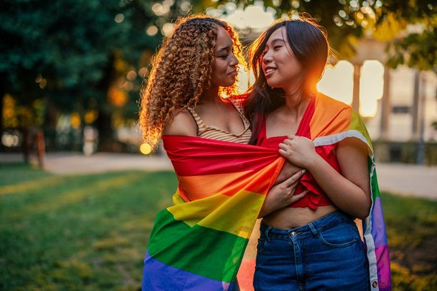 Two women looking at each other while having a pride flag wrapped around their shoulders