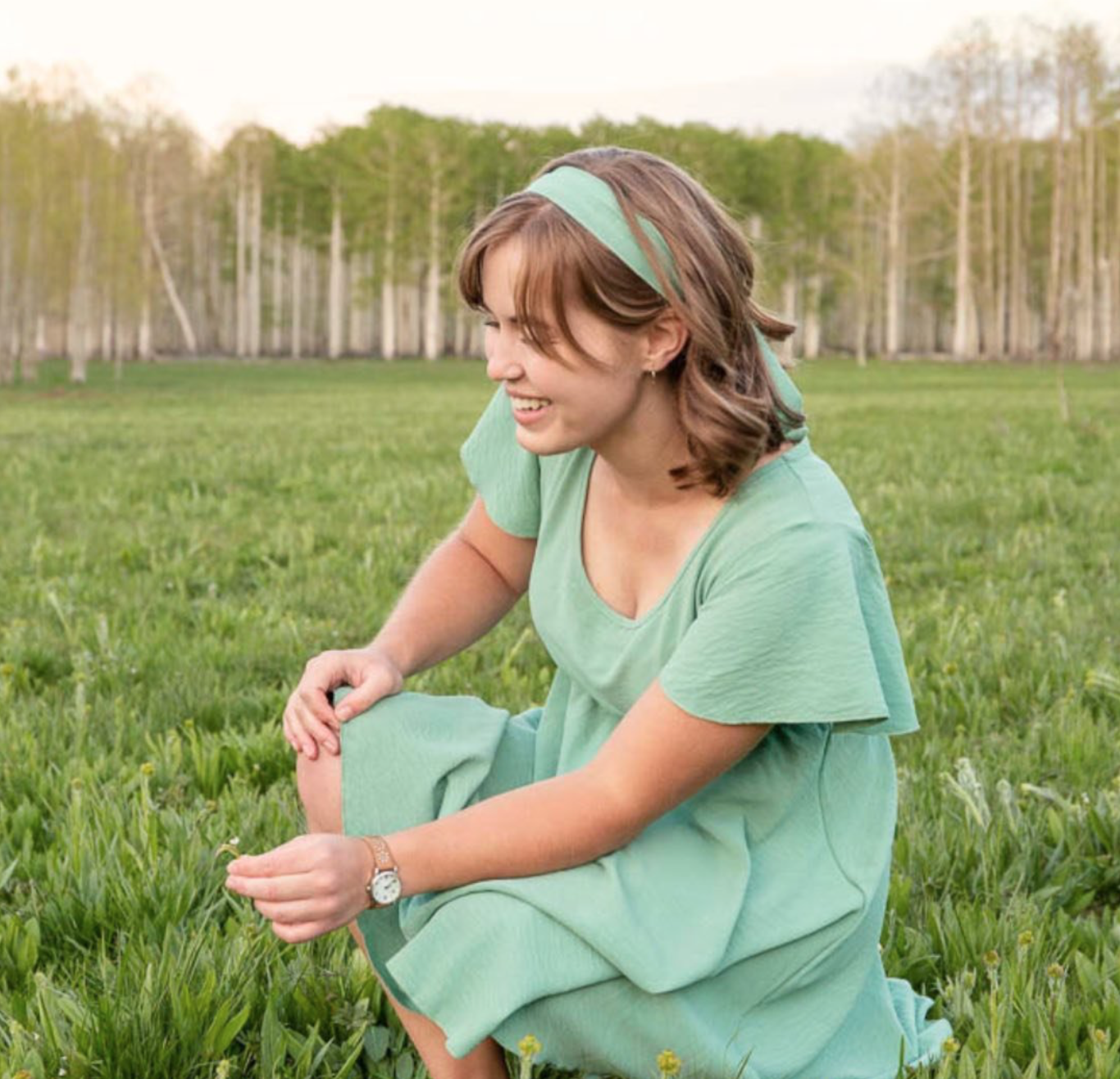 an image of the site creator, Angel Miller, weaaring a green dress and headband, bending down to pick a flower.