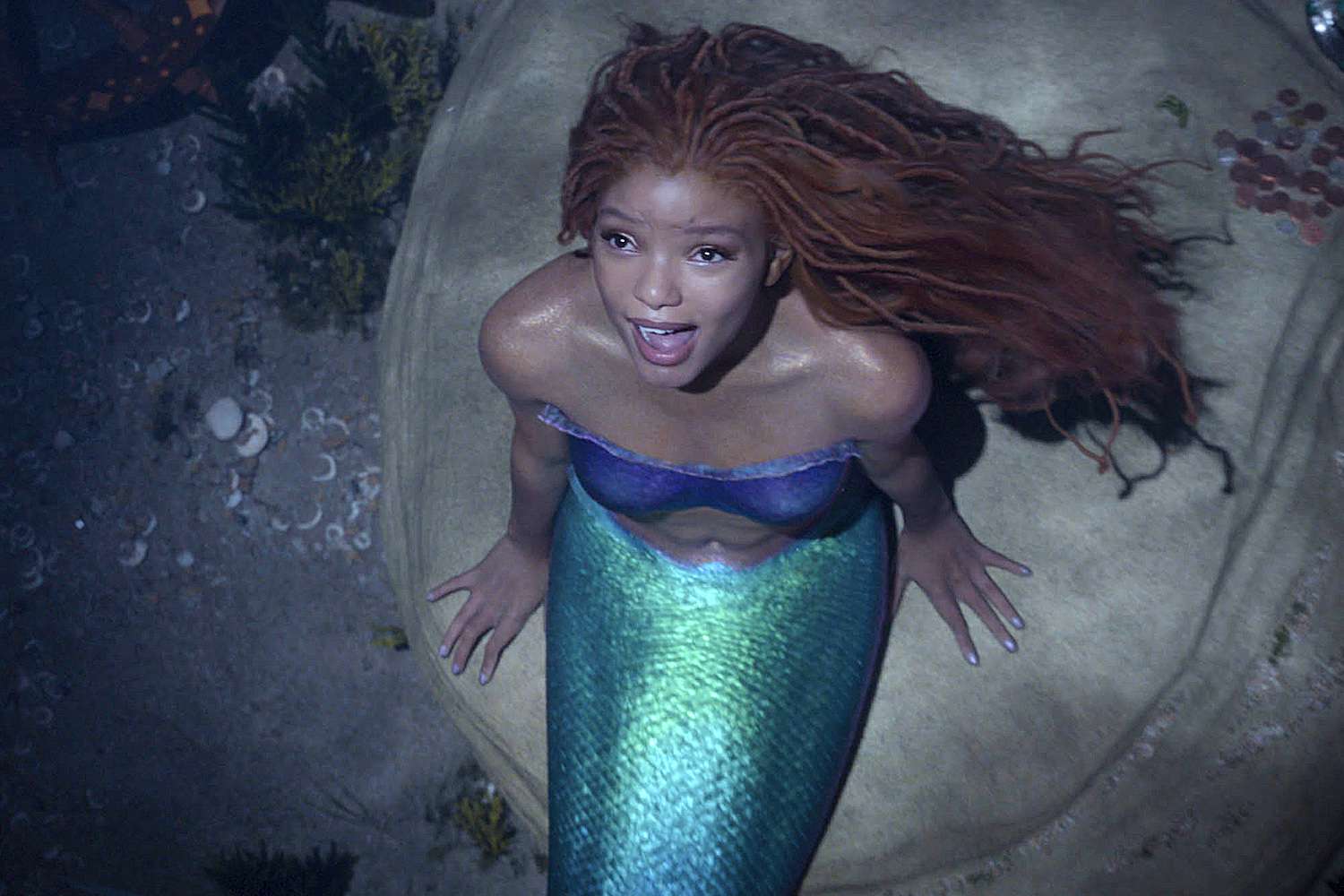 a photo of the 2023 The Little Mermaid during the song 'Part of Your World.' It features Ariel on a rock under the sea, looking up at the sun in her cave.