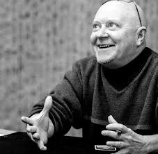 A black and white picture of Christopher Rush smiling, with open arms, looking up.