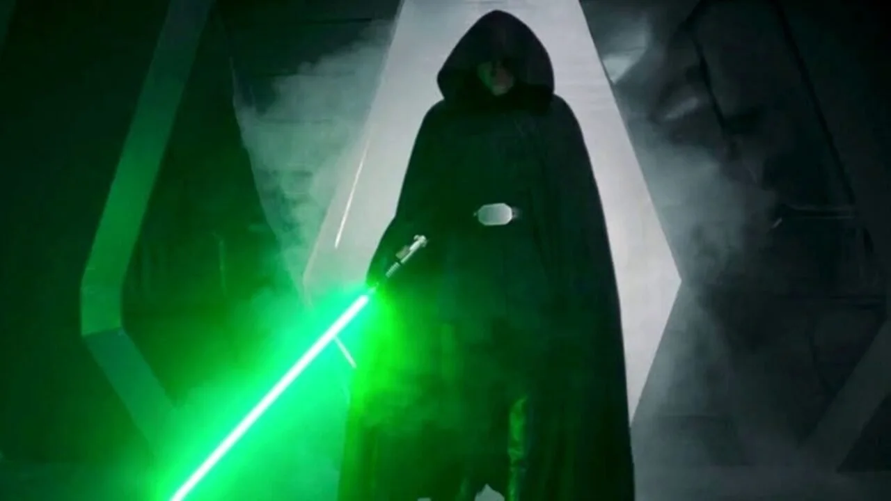 a photo of Luke Skywalker in his Episode 6 garb with a green lightsaber in hand, out to the side, his black hood up, obscuring the face.