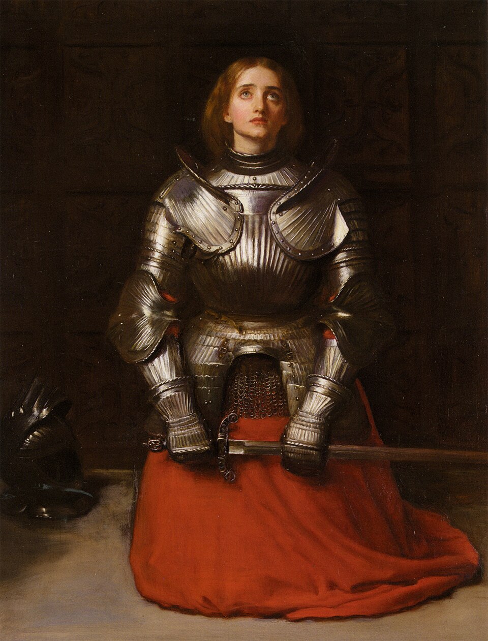 A painting depicts a woman in medieval-style, steel armor. She is kneeling at the center of the painting on a stone ground with dark, oak walls behind her. On her  lap is a bright red fabric and her hands, which are clasping a sword. She looks up with a somber and concerned expression.