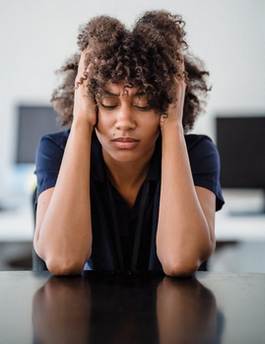 A picture of a woman sitting at a desk with her head in her hands looking sad or exausted.