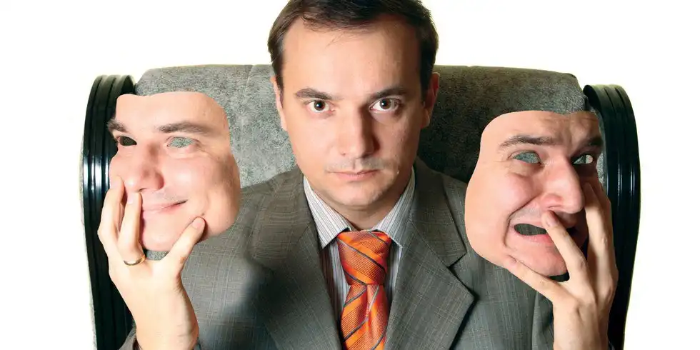 A man in a suit holding two masks each with different emotions