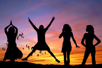 a silouette image of four woman, each in a different pose. In order from left to right their poses are; hands together above her head, jumping while making an x shape with her body, holding one hand to her mouth, both hands on her hips. In the background there are birds flying and a colorful sunset