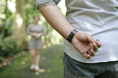an image of a person in the foreground holding an engagement ring behind their back, facing an out of focus person in the background