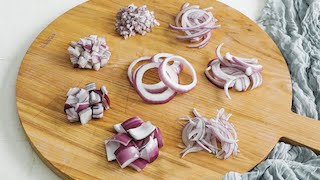 A circular cutting board with different preparations of red onions. In the center, the onions are moderately sliced and left round. At approximately the 2 o'clock position they are julienned. At approximately the 3 o'clock position they are julienned slightly thicker. At approximately the 5 o'clock position they are julienned thinner. At approximately the 7 o'clock position they are cubed. At approximately the 8 o'clock position they are diced. At approximately the 9 o'clock position they are diced smaller. At approximately the 11 o'clock position they are minced.